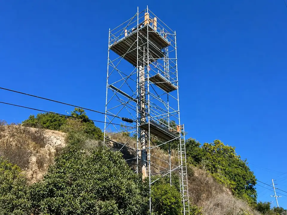 Tall scaffold tower on a dry, brushy hillside under a blue sky