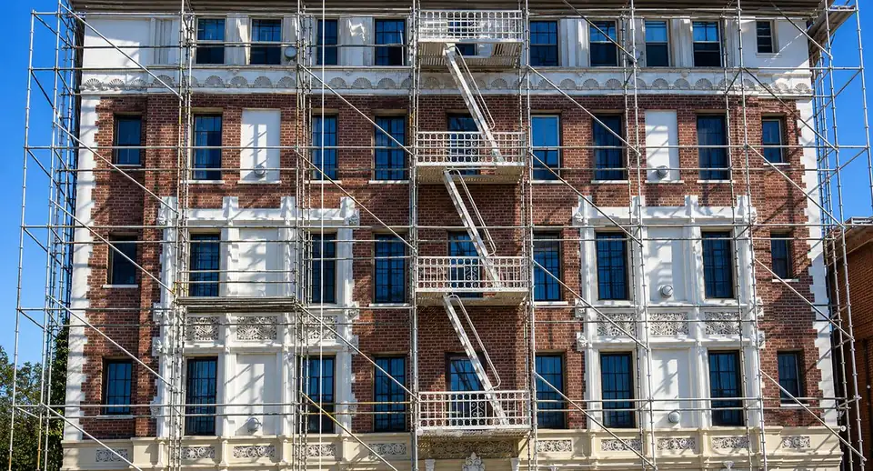 Scaffold covering the front of a historic brick building with ornate white window trim