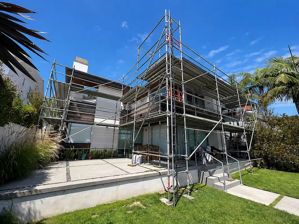 Scaffold around a modern two-story home with a lawn and palm trees