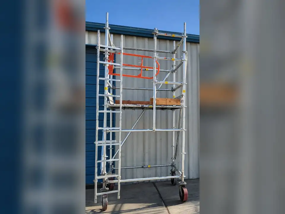 Aluminum rolling scaffold tower with guardrails set up beside a metal building