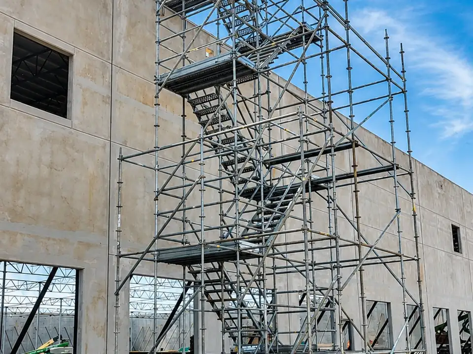 Scaffold stair tower with switchback stairs and guardrails against a tall concrete wall