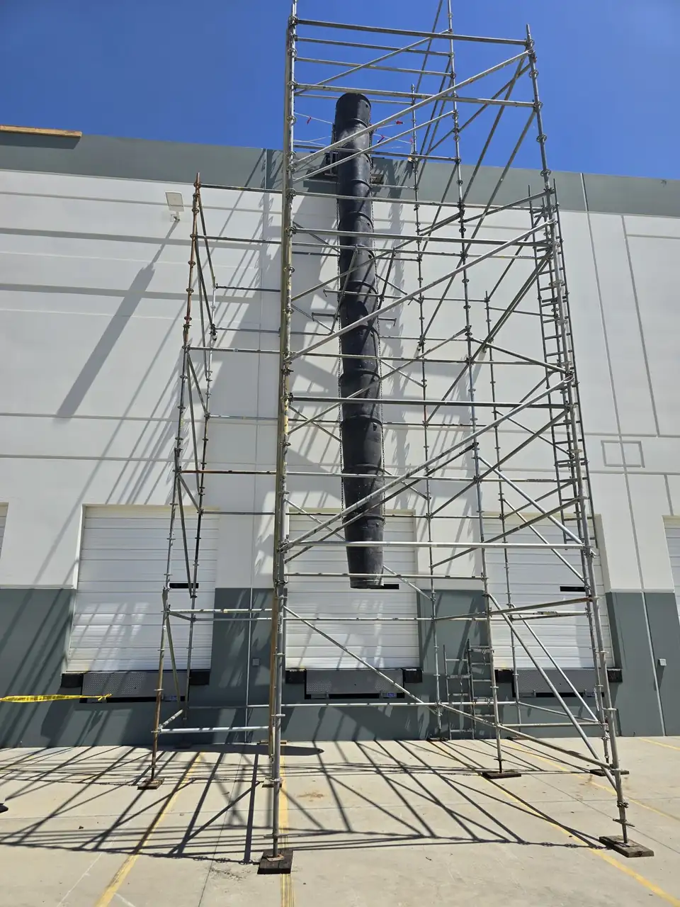 Scaffold tower holding a debris chute against a white warehouse wall