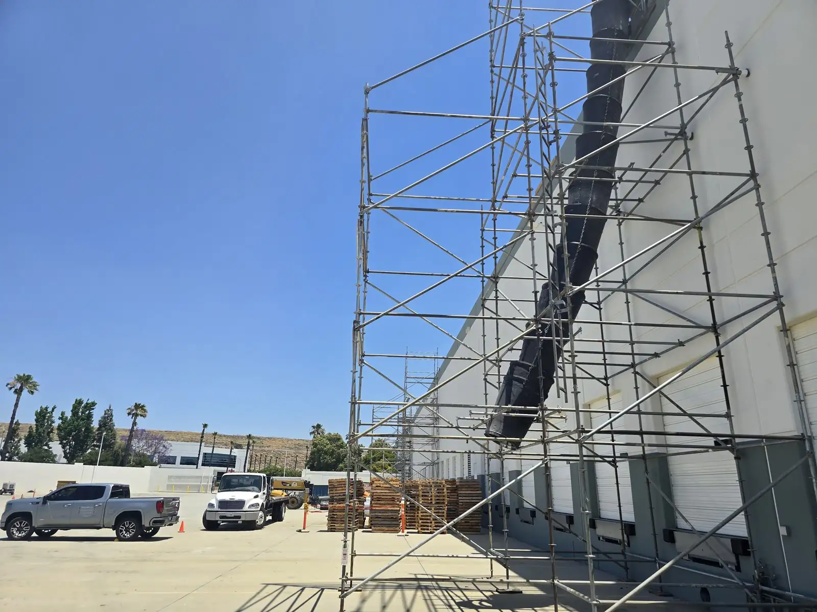 Tall scaffold running up the wall of a large warehouse with pickup trucks parked nearby